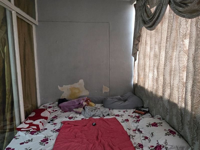 A bedroom featuring a glass partition wall and sliding door, currently showing signs of wall surface deterioration and peeling paint.