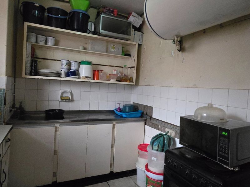 A compact kitchen featuring basic cabinetry, a stainless steel sink, and tiled backsplash, currently requiring significant cosmetic updates and maintenance to improve functionality.