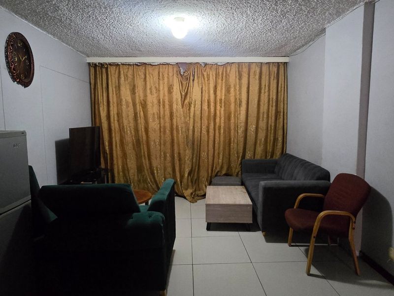A living room featuring tiled flooring and a textured ceiling, offering a functional space that could benefit from modern updates and improved lighting.