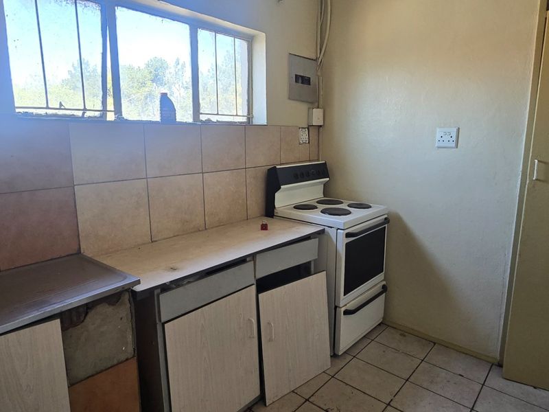 A dated kitchen featuring tiled flooring, a tiled backsplash, and a freestanding stove, currently requiring renovation and cabinet repairs.