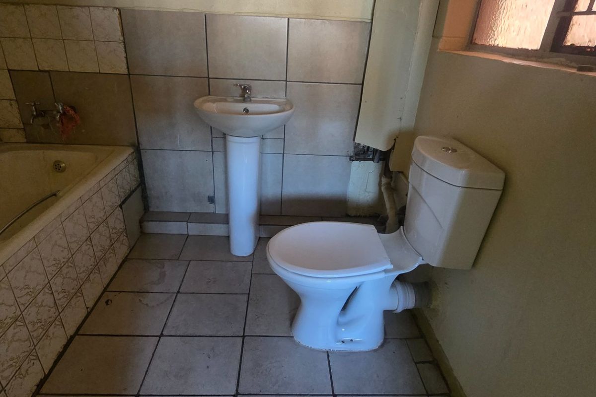 A dated bathroom featuring a pedestal basin, toilet, and bathtub with tiled surfaces, requiring renovation to update the finishes and address visible wear.