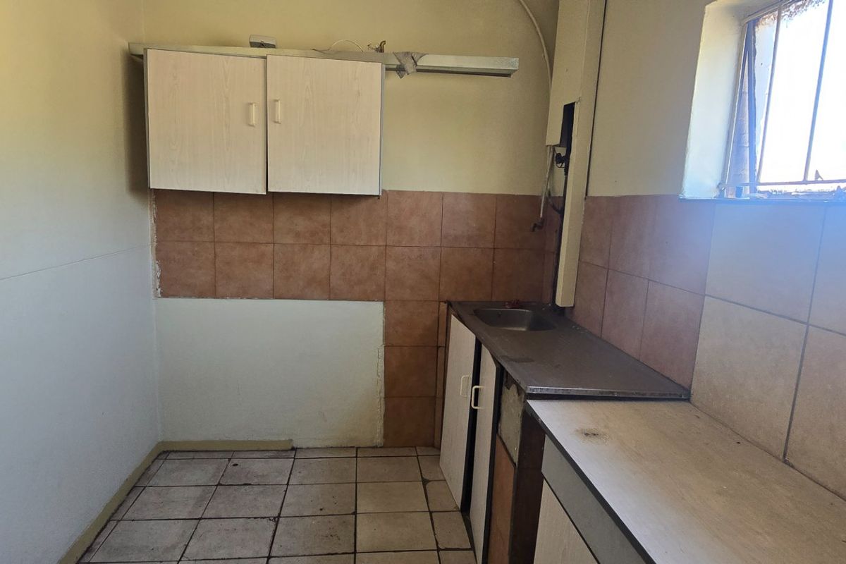 A compact kitchen space featuring built-in cabinetry, a stainless steel sink, and tiled splashbacks, currently requiring renovation and cosmetic updates.