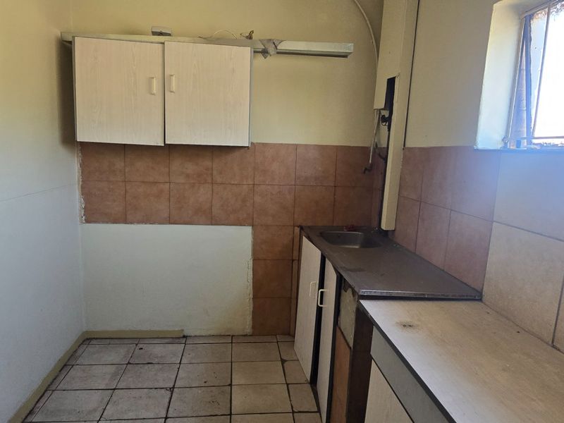 A compact kitchen space featuring built-in cabinetry, a stainless steel sink, and tiled splashbacks, currently requiring renovation and cosmetic updates.
