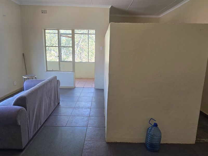 A living area featuring tiled flooring, large windows providing natural light, and a central partition wall, offering a functional layout for potential renovation.