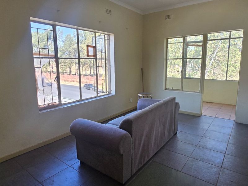 A living room area featuring tiled flooring and large steel-framed windows, offering natural light and a view of the exterior surroundings.