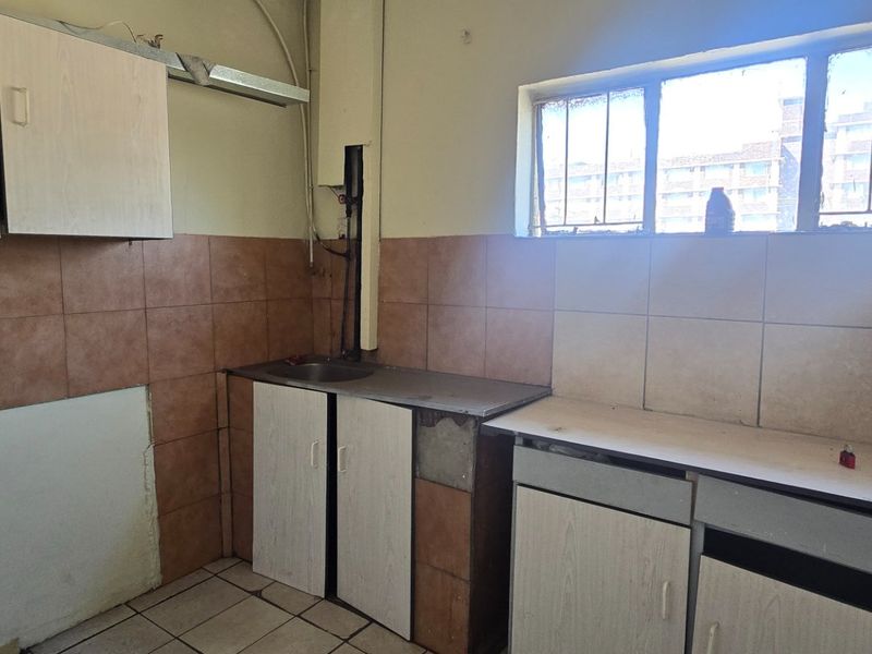A dated kitchen featuring original cabinetry, tiled splashbacks, and a stainless steel sink, requiring renovation to modernize the space.