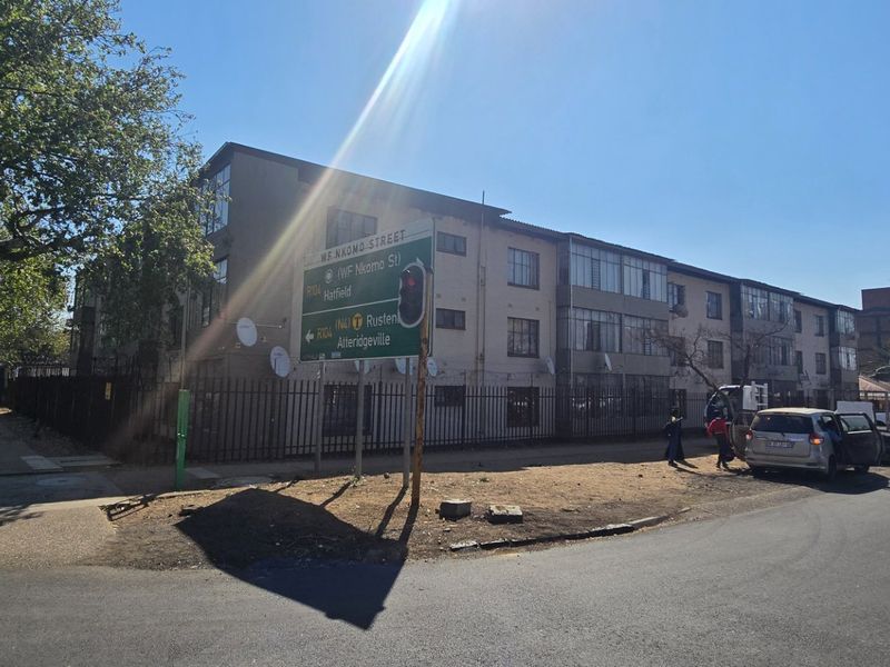 Street view of the apartment complex exterior, showing the building facade, security fencing, and surrounding road infrastructure.