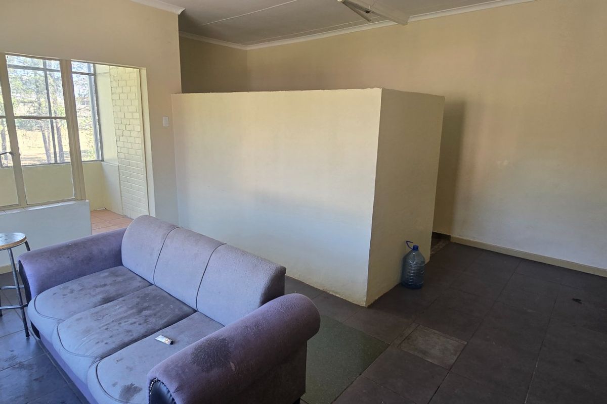 A living area featuring tiled flooring, a central partition wall, and natural light from a large window leading to an adjacent patio space.