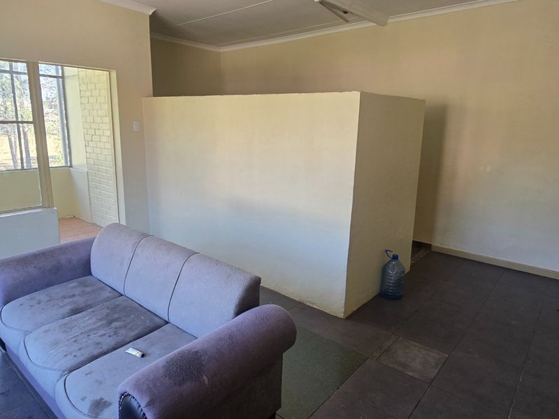 A living area featuring tiled flooring, a central partition wall, and natural light from a large window leading to an adjacent patio space.