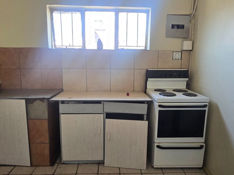 A dated kitchen area featuring basic cabinetry, a freestanding electric stove, tiled splashbacks, and a sink, requiring significant renovation and cosmetic updates.