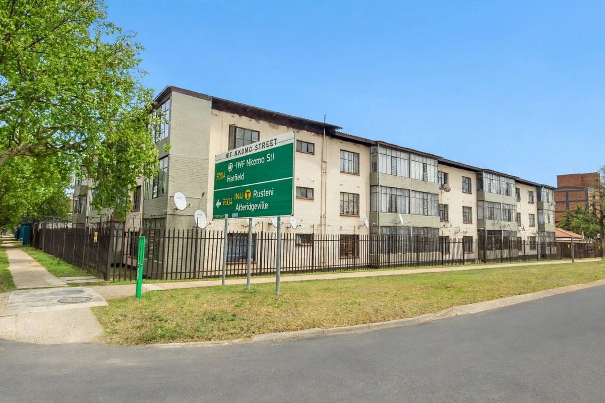 Street view of a multi-story apartment complex featuring enclosed balconies and secure perimeter fencing, situated on a corner lot.