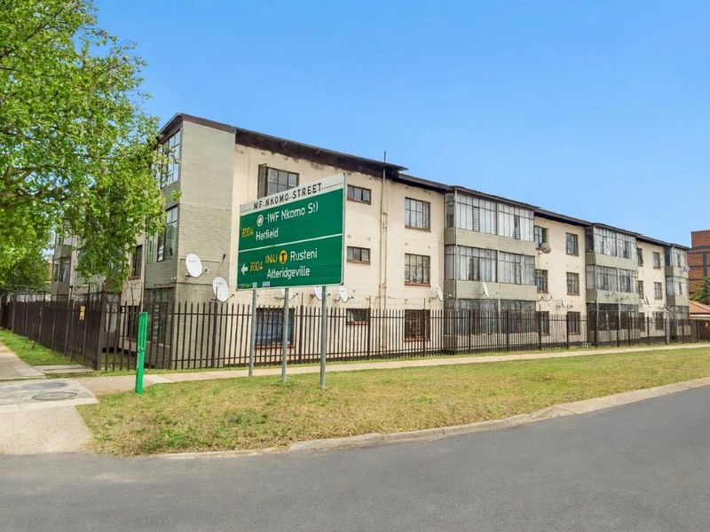 Street view of a multi-story apartment complex featuring enclosed balconies and secure perimeter fencing, situated on a corner lot.