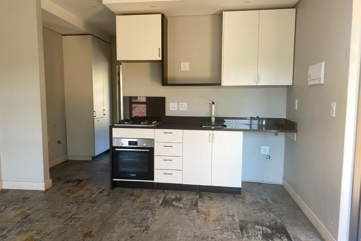A modern, compact kitchen featuring white cabinetry, dark stone countertops, a built-in oven, gas hob, and durable tiled flooring in an open-plan layout.