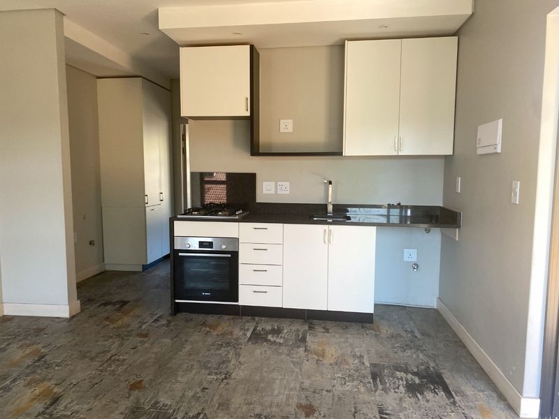 A modern, compact kitchen featuring white cabinetry, dark stone countertops, a built-in oven, gas hob, and durable tiled flooring in an open-plan layout.