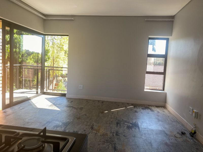 An open-plan living area featuring modern tiled flooring, large sliding doors leading to a balcony, and a built-in gas hob.