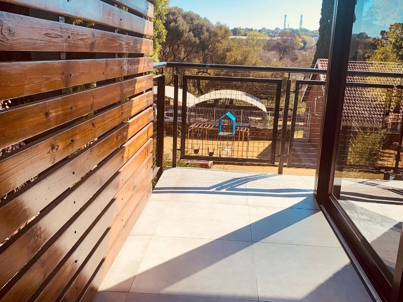 A modern balcony featuring tiled flooring, a timber slat privacy screen, and a metal balustrade, offering an open view of the surrounding area.
