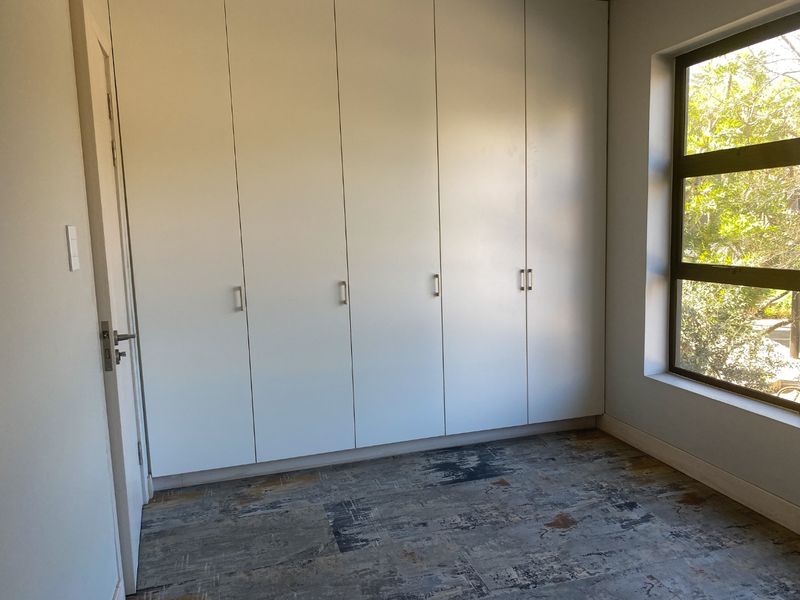 A bright, empty bedroom featuring extensive floor-to-ceiling built-in cupboards, modern tiled flooring, and a large window providing natural light.