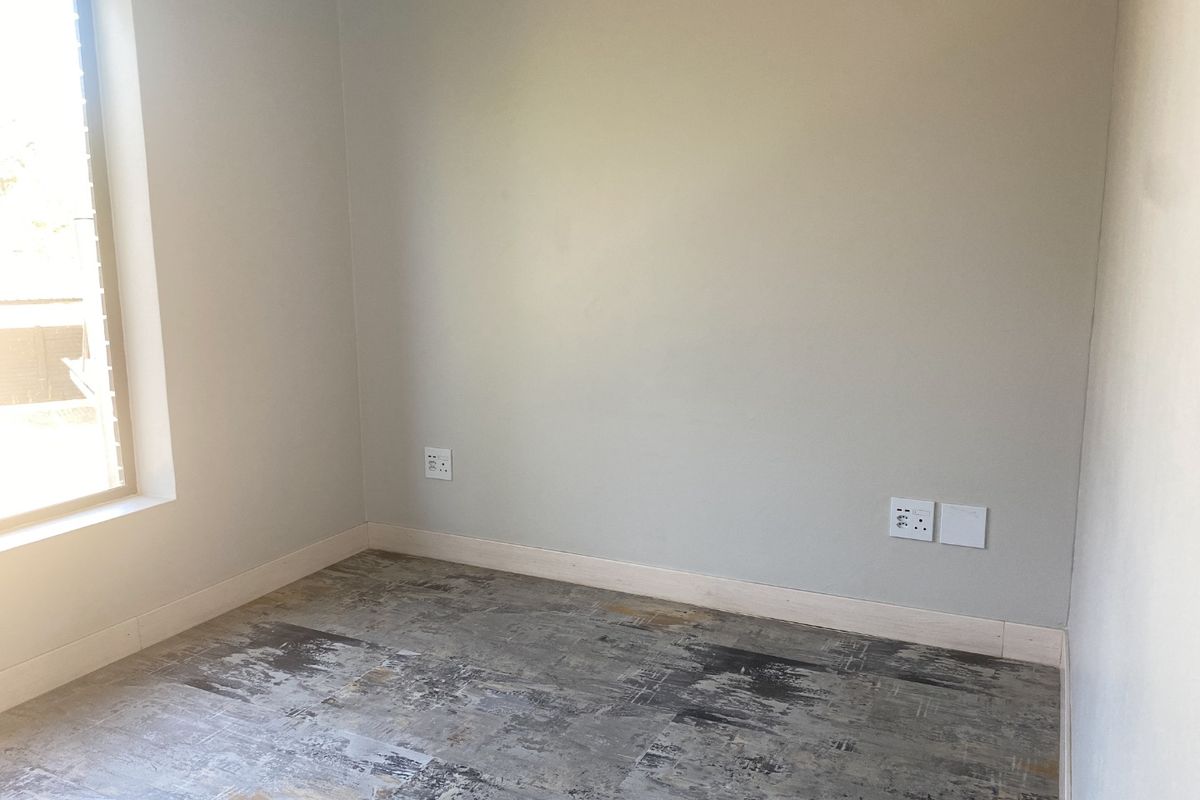An empty bedroom featuring neutral walls, modern patterned flooring, and natural light from a side window.
