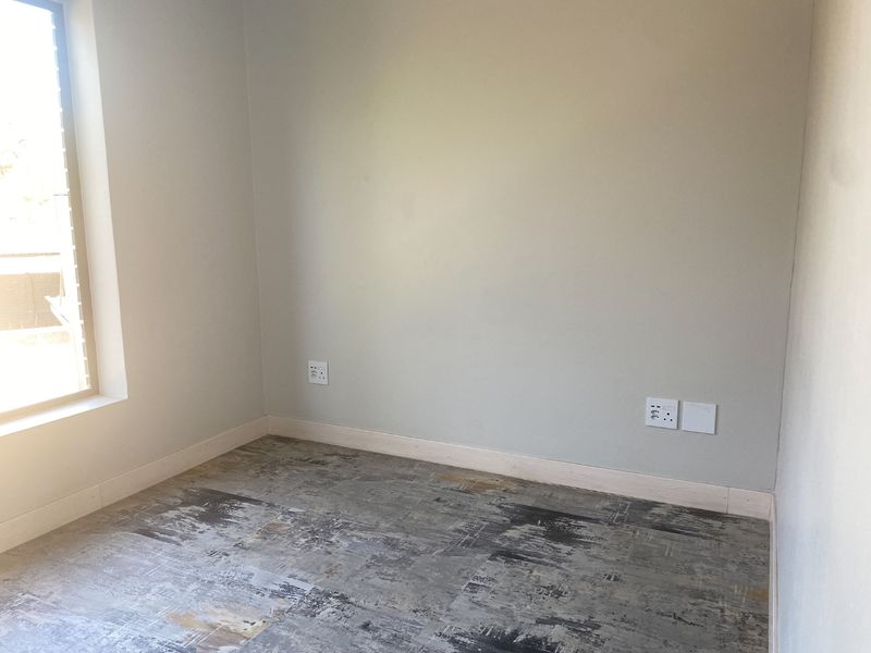 An empty bedroom featuring neutral walls, modern patterned flooring, and natural light from a side window.