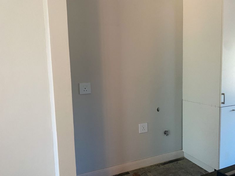 A dedicated laundry utility space featuring plumbing connections, electrical outlets, and adjacent built-in cabinetry, currently awaiting final flooring installation.