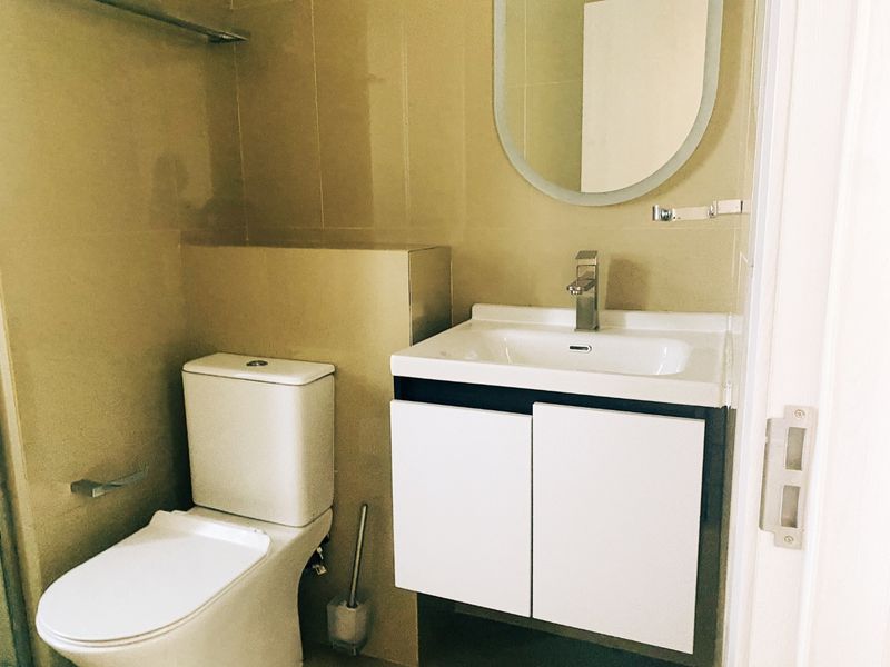 A clean, modern bathroom featuring a white vanity cabinet with basin, wall-mounted mirror, and standard toilet suite.