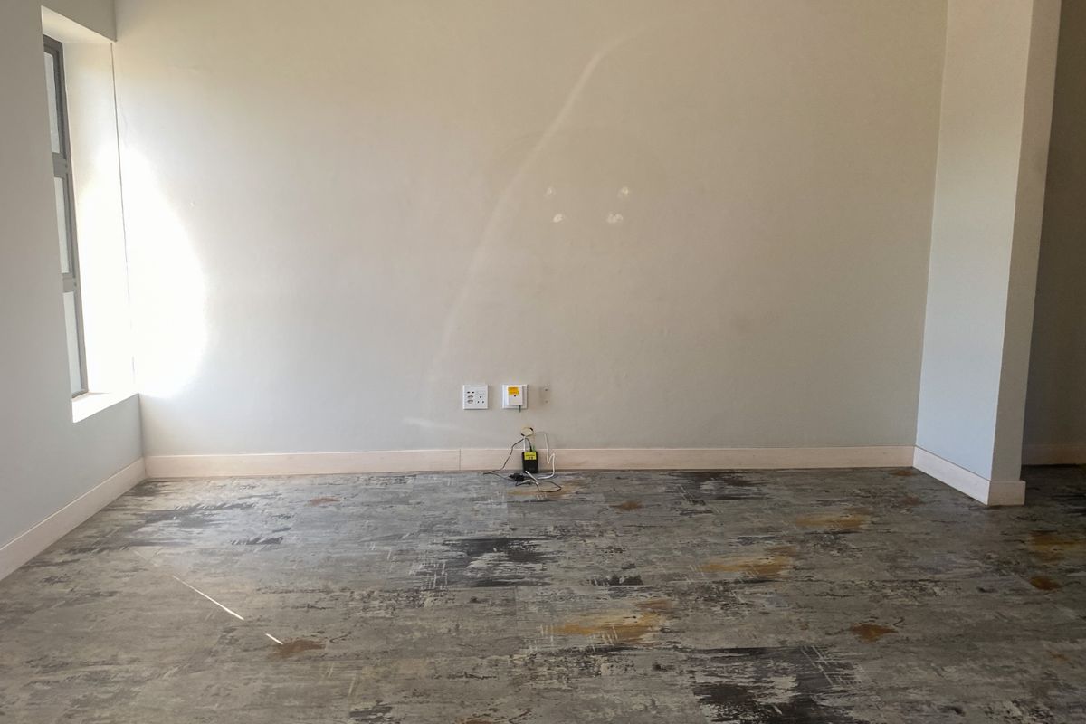 An empty living room area featuring textured flooring, neutral walls with electrical points, and a side window, ready for personalization.