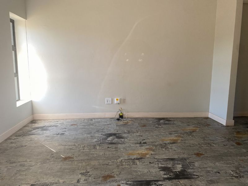 An empty living room area featuring textured flooring, neutral walls with electrical points, and a side window, ready for personalization.