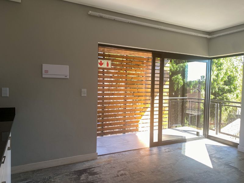 Open plan living area featuring large sliding glass doors leading to a private balcony with a timber privacy screen.