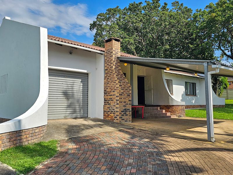 Front exterior view of the house featuring a brick chimney, roller garage door, and a covered carport area with paved driveway.