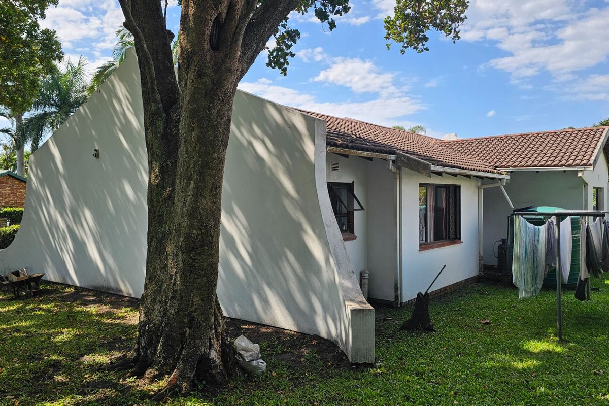 Rear exterior view of the house featuring a tiled roof, concrete parapet wall, and a water tank in the garden area.