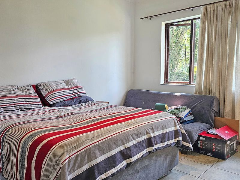 A functional bedroom featuring tiled flooring and windows fitted with security bars, providing a neutral space ready for personalization.
