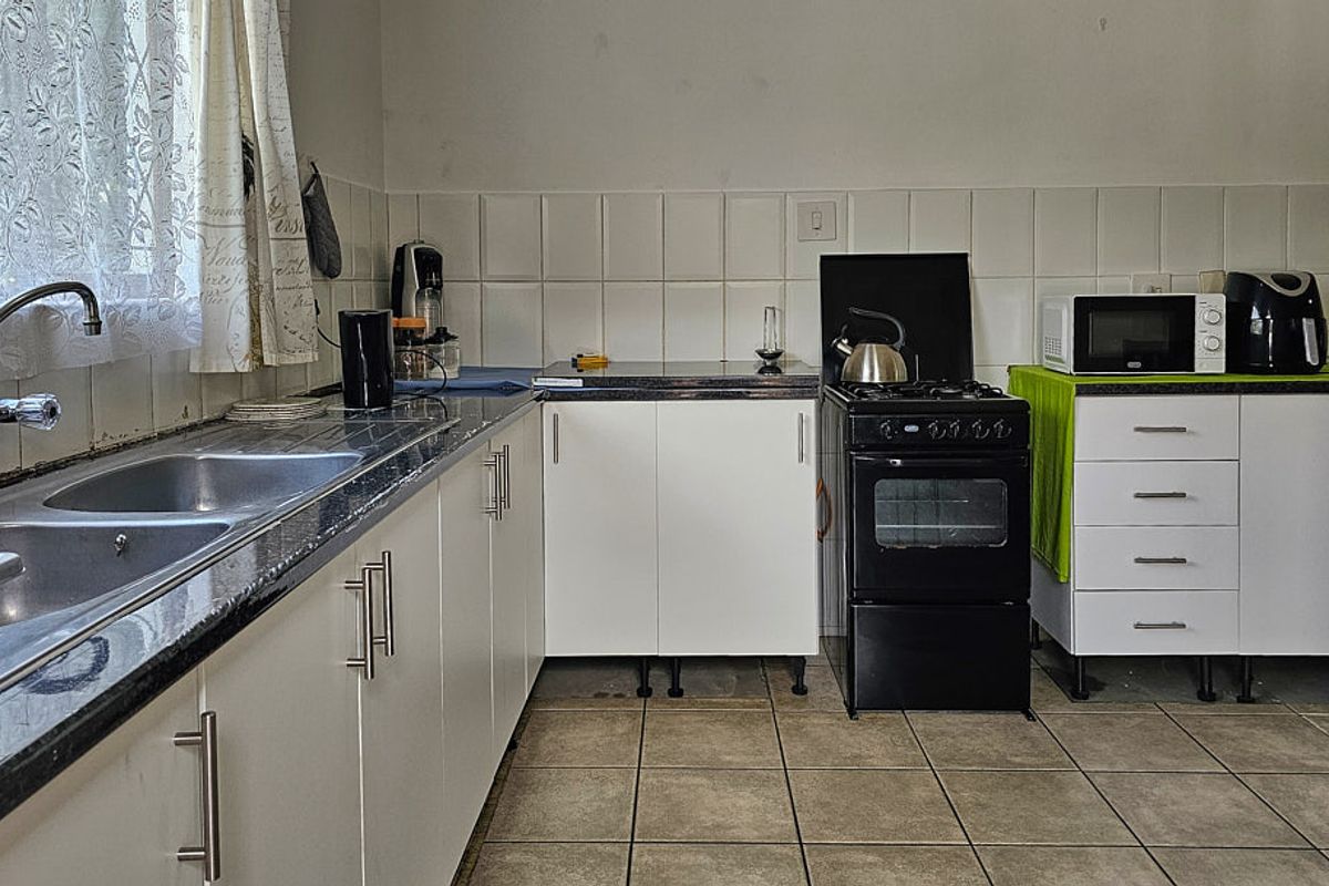 A functional kitchen featuring white cabinetry, laminate countertops, a double stainless steel sink, and a freestanding gas stove with tiled backsplash and flooring.