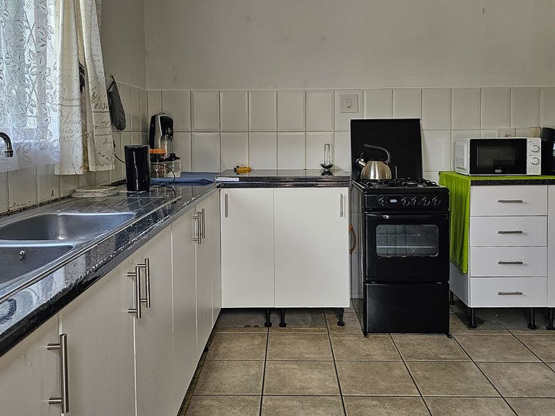 A functional kitchen featuring white cabinetry, laminate countertops, a double stainless steel sink, and a freestanding gas stove with tiled backsplash and flooring.