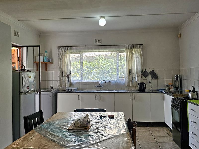 Functional kitchen featuring white built-in cabinetry, tiled backsplash, double sink, and tiled flooring, offering a practical layout for daily meal preparation.