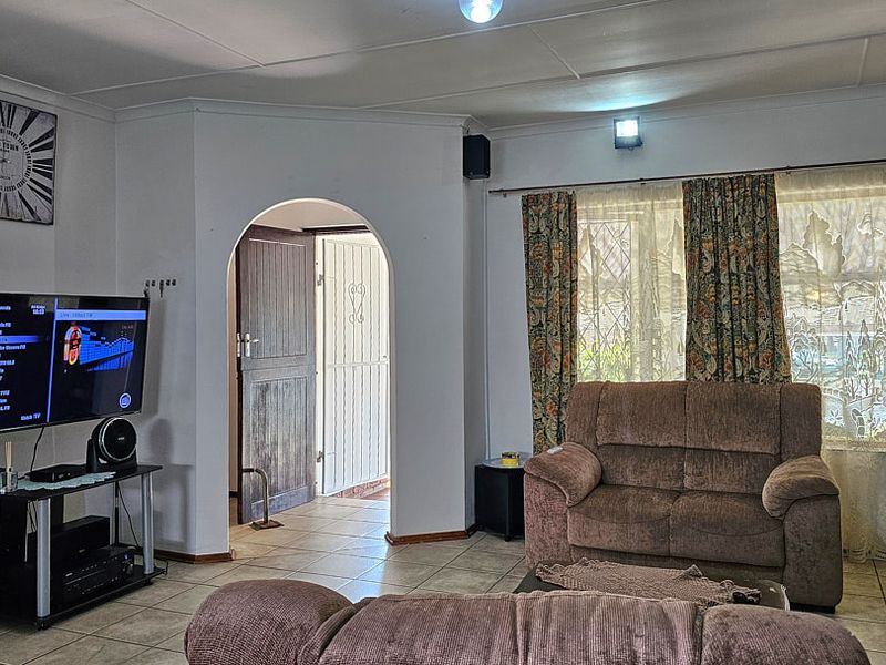A living room featuring tiled flooring, an arched doorway leading to the entrance, and natural light through window treatments.