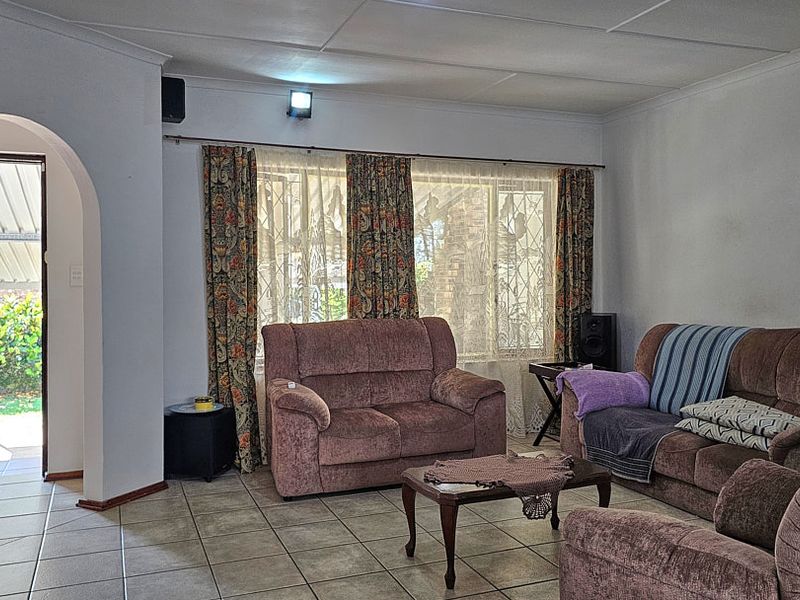 A living room featuring tiled flooring, a coved ceiling, and an arched doorway leading to an outdoor area with a security gate.