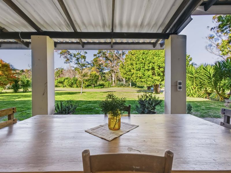 A covered outdoor patio area featuring structural pillars and a corrugated roof, overlooking a spacious green garden.
