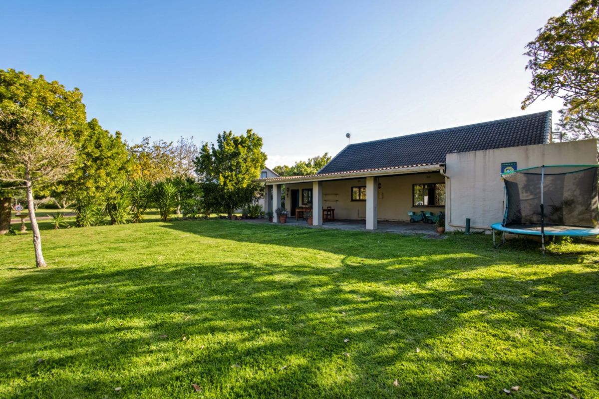 A spacious rear garden featuring a well-maintained lawn and a covered patio area with concrete pillars, providing an ideal space for outdoor relaxation.