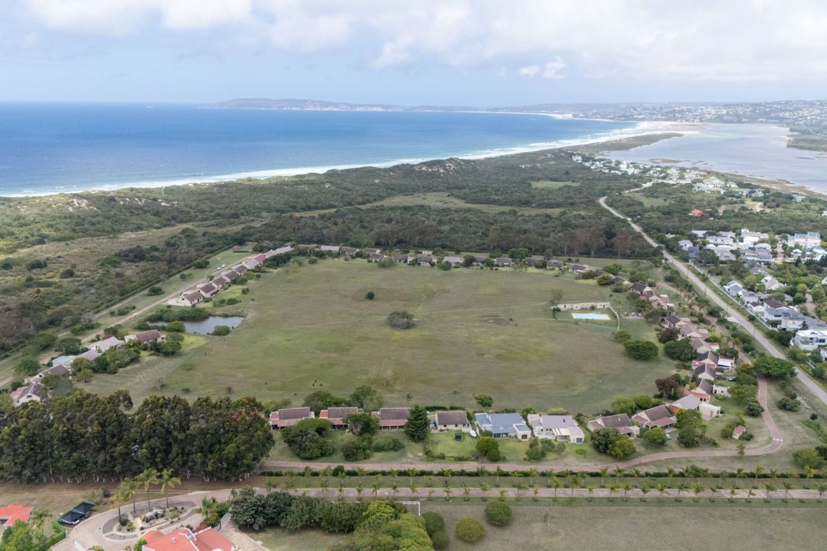 An aerial view of a coastal residential estate featuring multiple dwellings, open green spaces, and proximity to the ocean and lagoon.