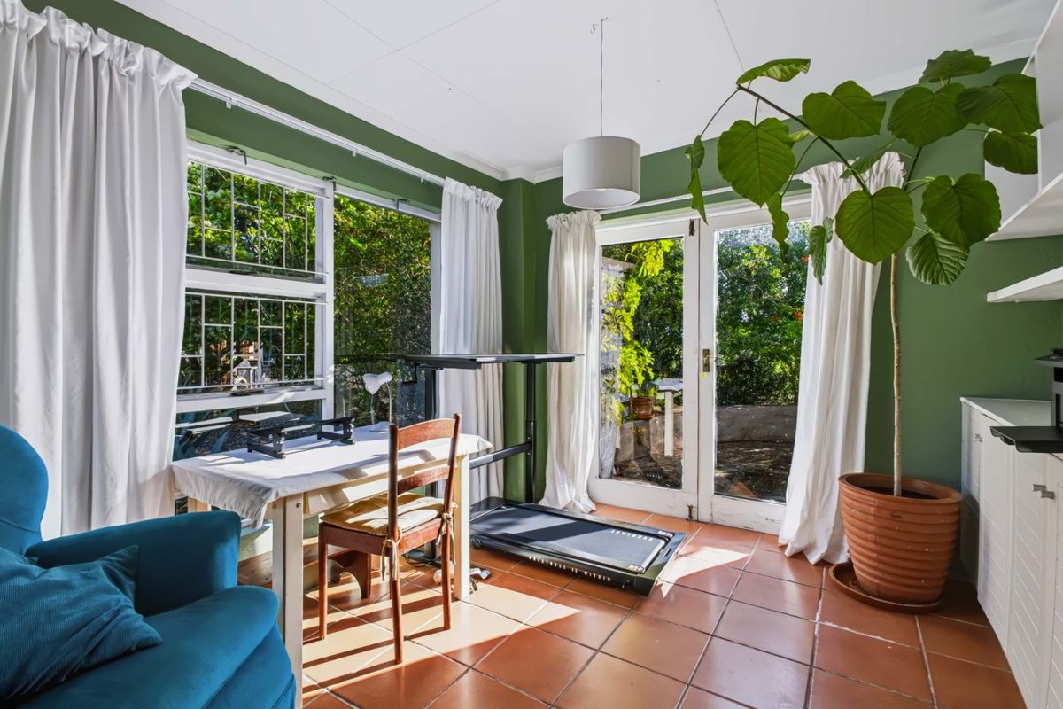 Sunlit living area featuring terracotta floor tiles, large windows, and direct access to the garden through classic french doors.