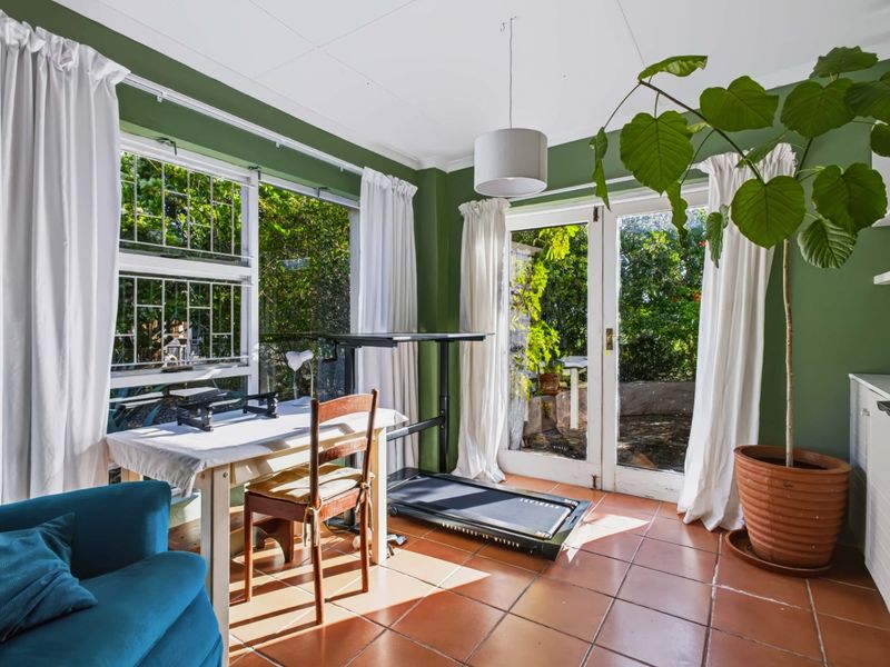 Sunlit living area featuring terracotta floor tiles, large windows, and direct access to the garden through classic french doors.