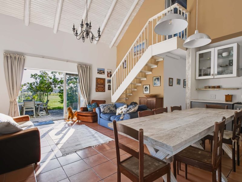 Spacious open-plan living and dining area featuring a vaulted ceiling, tiled floors, a staircase, and direct access to an outdoor patio.