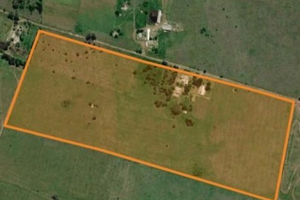 An aerial view of a large, open farm plot with a clearly defined boundary, featuring expansive grazing land and scattered vegetation.