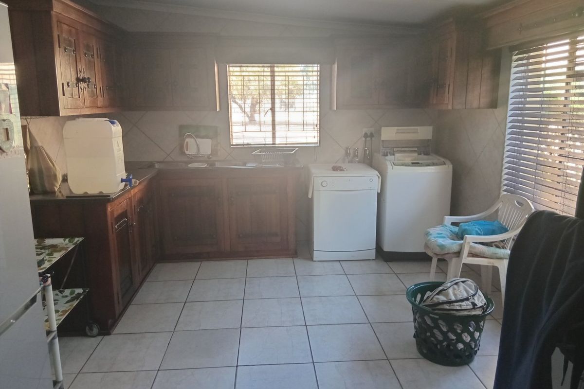 A functional kitchen featuring wooden cabinetry, tiled flooring, and a tiled backsplash, with space for laundry appliances and natural light from the window.