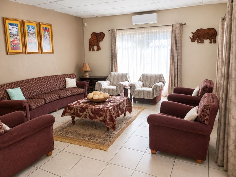 A spacious living room featuring tiled flooring, a drop ceiling, and a wall-mounted air conditioning unit, providing a comfortable and functional living space.
