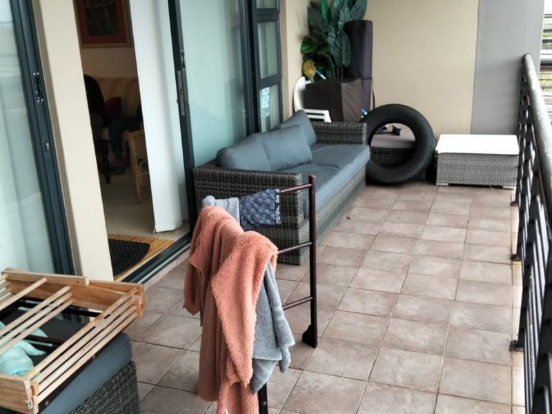 A covered balcony featuring tiled flooring, a metal balustrade, and sliding glass door access to the interior living space.