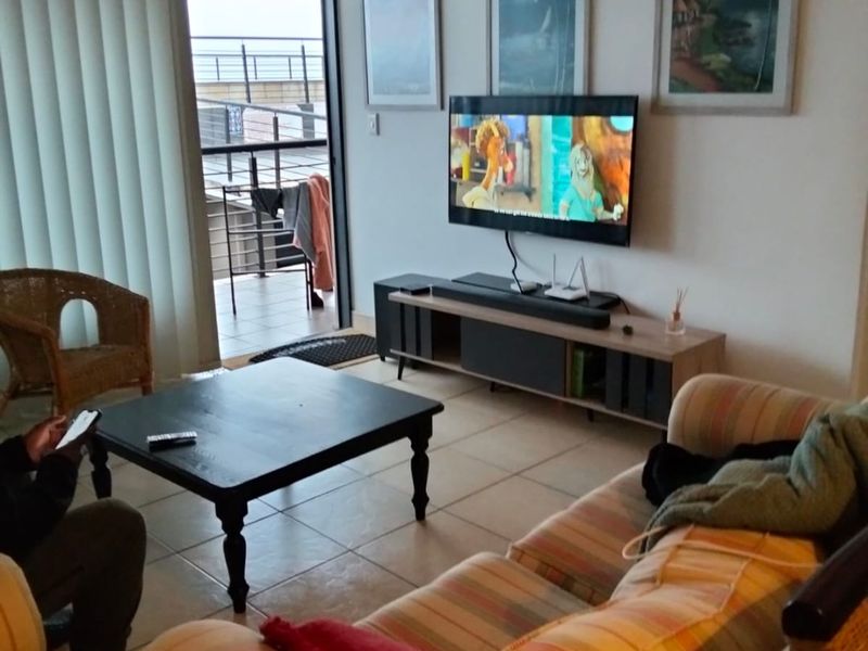 A comfortable living room featuring tiled flooring, a wall-mounted air conditioning unit, and direct access to an outdoor balcony through a sliding glass door.