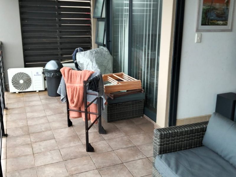 A covered balcony featuring tiled flooring, sliding glass door access, and a privacy screen, providing an outdoor extension to the living area.