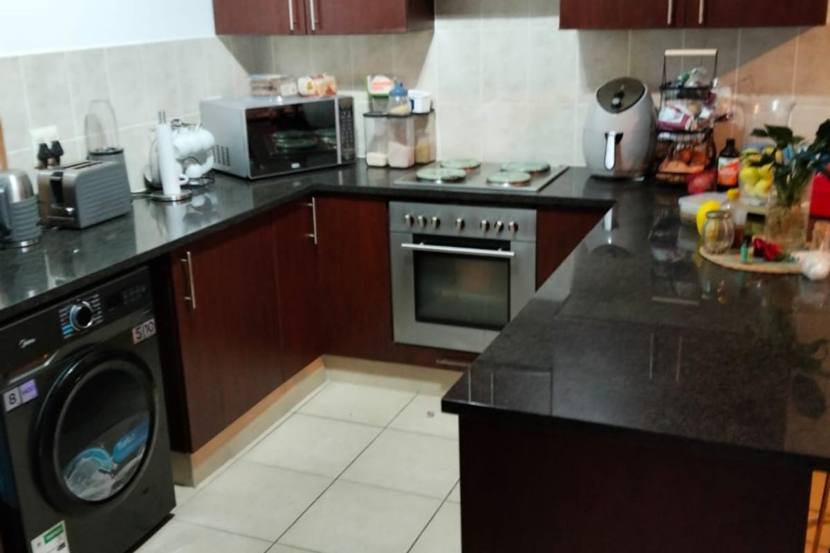 A functional kitchen featuring dark wood cabinetry, granite countertops, integrated oven and hob, and tiled flooring with a breakfast bar area.
