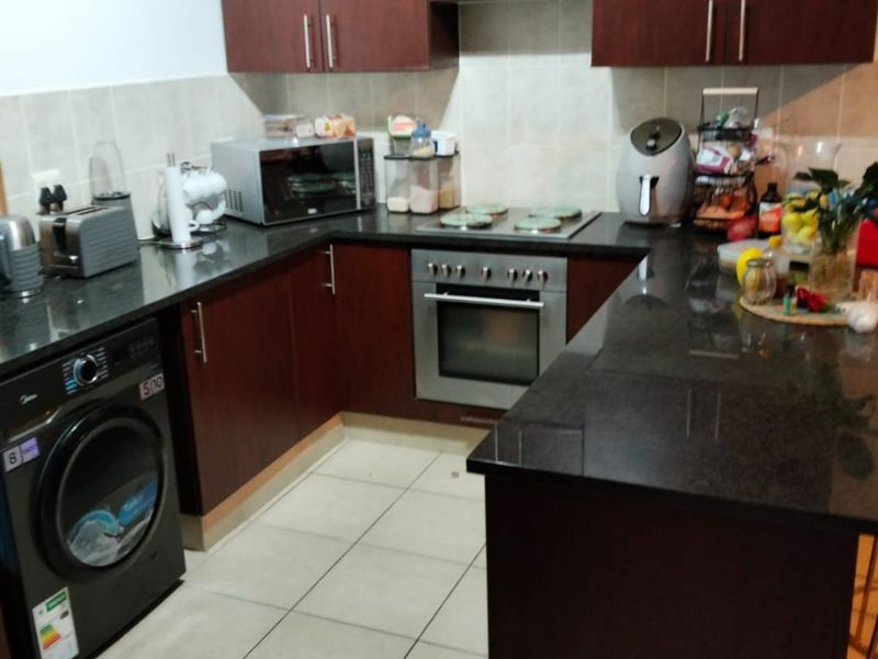 A functional kitchen featuring dark wood cabinetry, granite countertops, integrated oven and hob, and tiled flooring with a breakfast bar area.